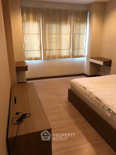 Cozy bedroom with wooden flooring and natural light through large windows.