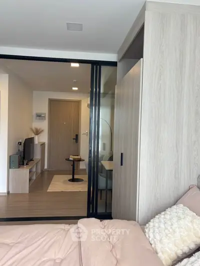 Modern bedroom with sliding glass doors leading to a cozy living area, featuring stylish decor and wooden flooring.