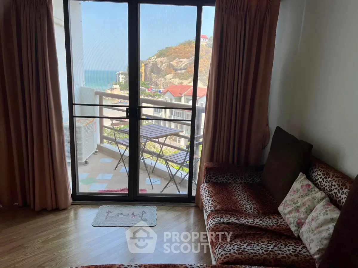 Cozy living room with balcony offering stunning ocean and mountain views, perfect for relaxation.