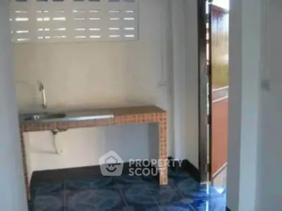 Compact kitchen area with tiled countertop and sink, featuring an open door for natural light.