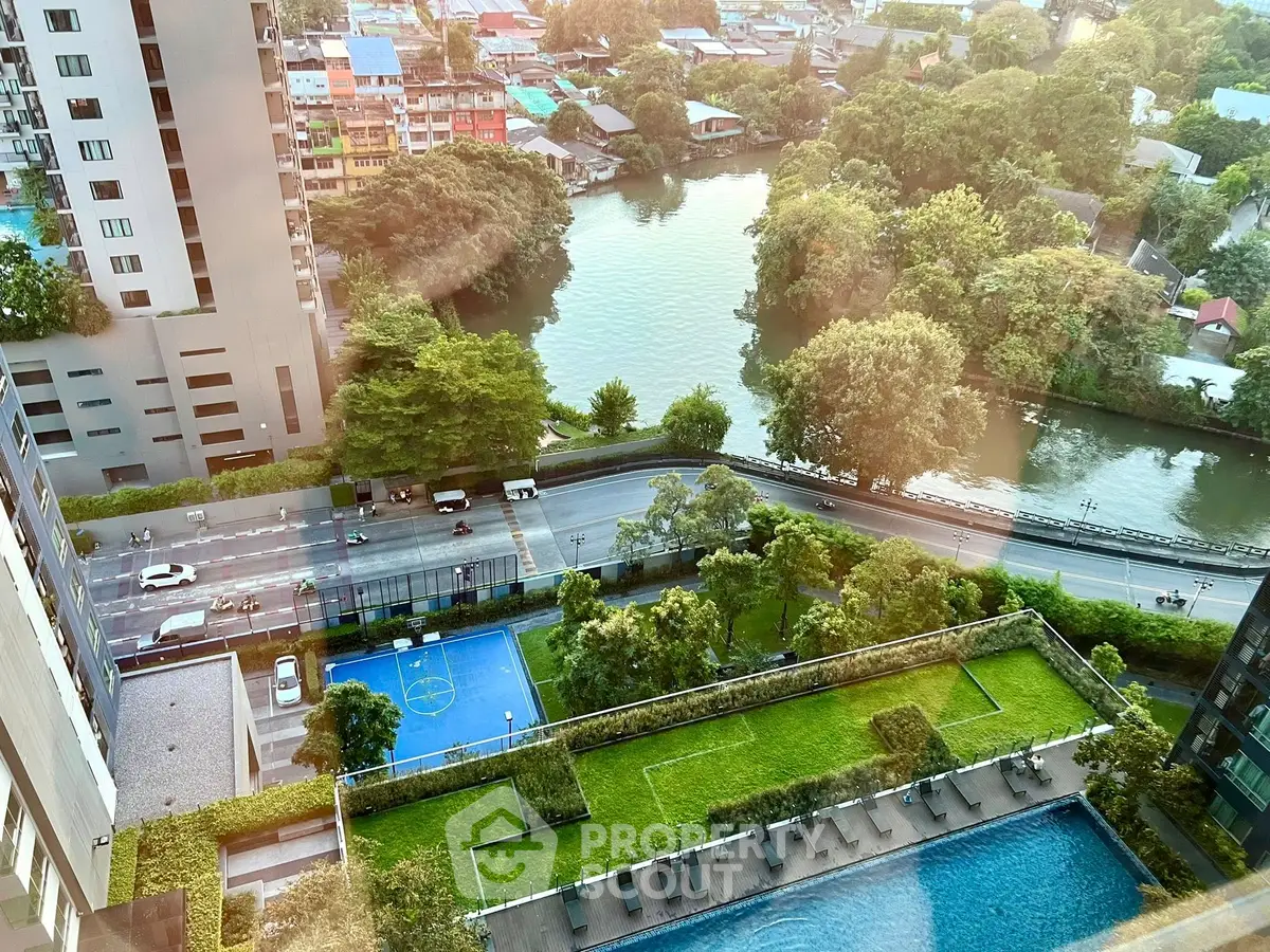Stunning high-rise view with pool, garden, and sports court overlooking a serene river.