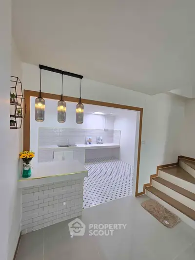 Modern kitchen with stylish lighting and open layout, featuring white tiles and sleek countertops.