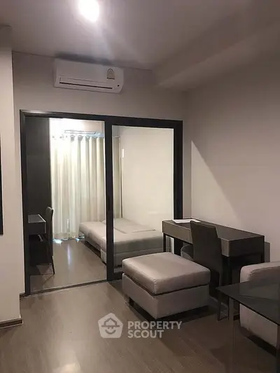 Modern living room with sleek furniture and glass partition leading to a cozy bedroom.
