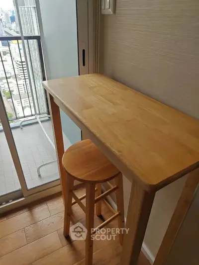 Cozy balcony with wooden table and stool offering city views, perfect for relaxation.