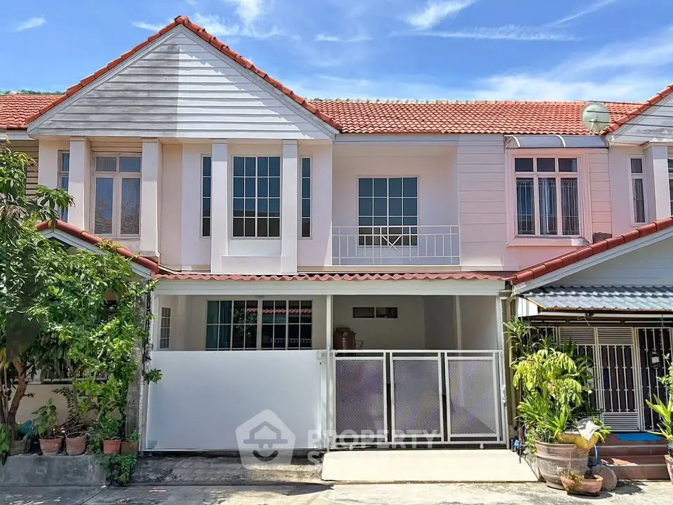 Charming two-story house with red roof and gated entrance, ideal for family living.