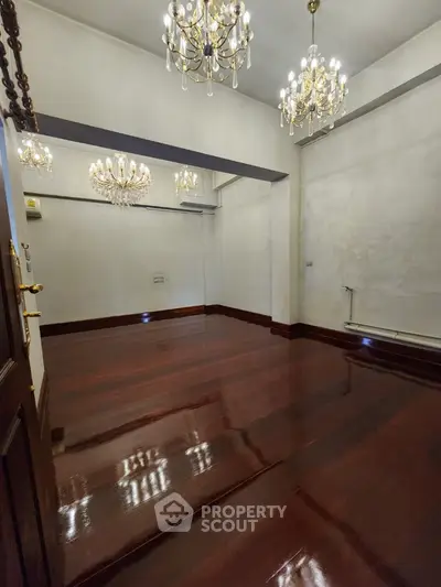 Elegant empty room with polished wooden floors and chandeliers, perfect for luxury living.