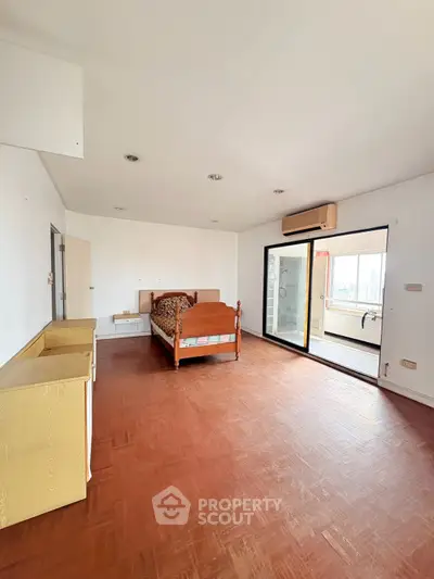 Spacious bedroom with wooden flooring and large windows leading to a balcony with city views.