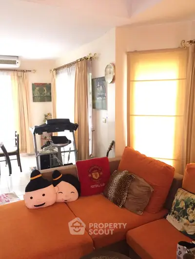 Cozy living room with bright orange sofa and natural light, perfect for relaxation and entertaining.