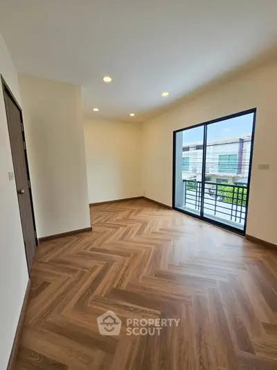 Spacious room with elegant wooden flooring and large window offering natural light and balcony access.