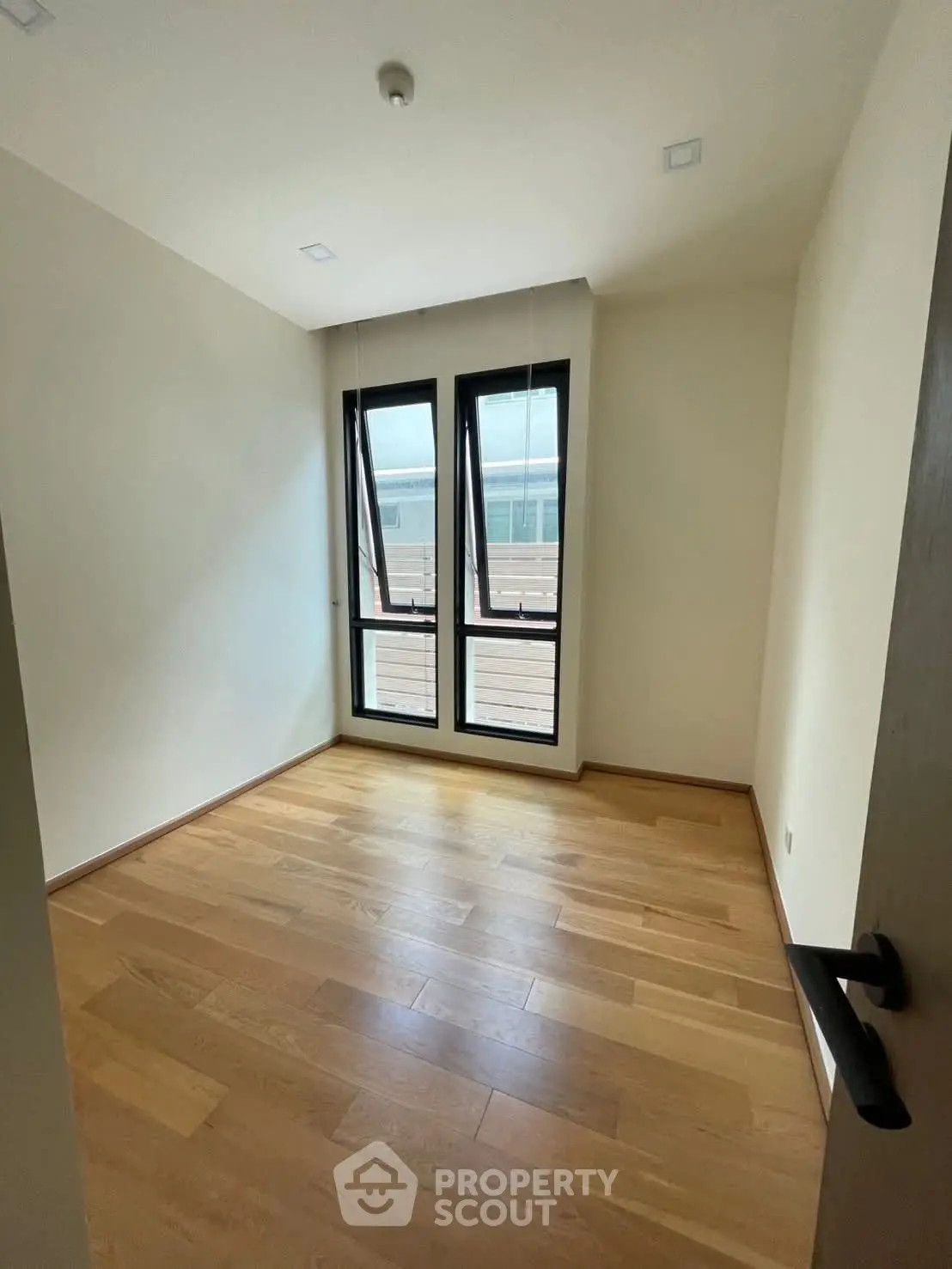 Spacious empty room with wooden flooring and large windows for natural light.