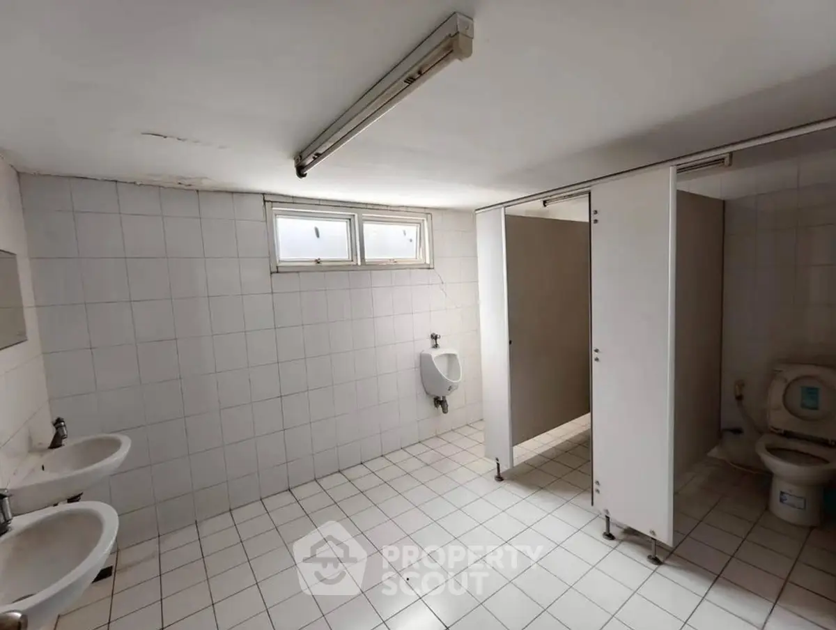 Spacious commercial bathroom with tiled walls and floors, featuring dual sinks and a urinal.