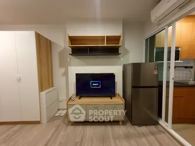 Modern living room with sleek furniture and kitchen view, featuring a TV and refrigerator.