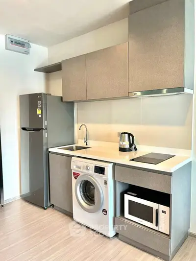 Modern kitchen with sleek appliances including washing machine, microwave, and fridge in compact layout.