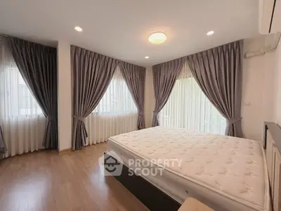 Spacious bedroom with large windows and elegant curtains, featuring a comfortable bed and wooden flooring.