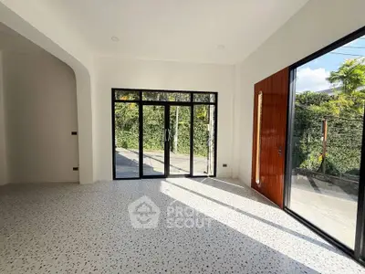 Spacious living room with large windows and terrazzo flooring, offering abundant natural light and garden views.