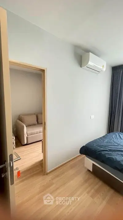 Modern bedroom with air conditioning and wooden flooring, adjacent to a cozy living area.