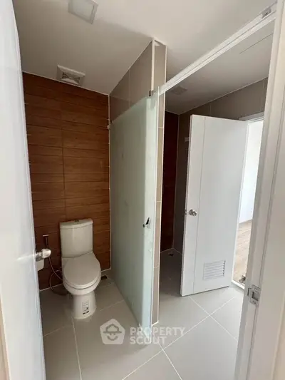 Modern bathroom with sleek design and wooden accent wall, featuring a toilet and frosted glass door.