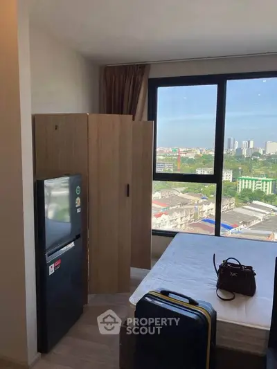 Cozy bedroom with city view, featuring a compact fridge and stylish decor, perfect for urban living.