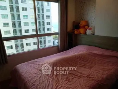 Cozy bedroom with large window offering city view, featuring a plush teddy bear on the bed.