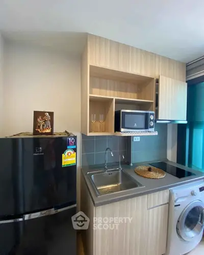 Modern compact kitchen with fridge, microwave, and washing machine in a stylish apartment.