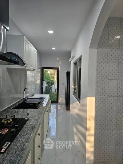 Modern kitchen with sleek countertops and gas stove, leading to a garden view through a glass door.