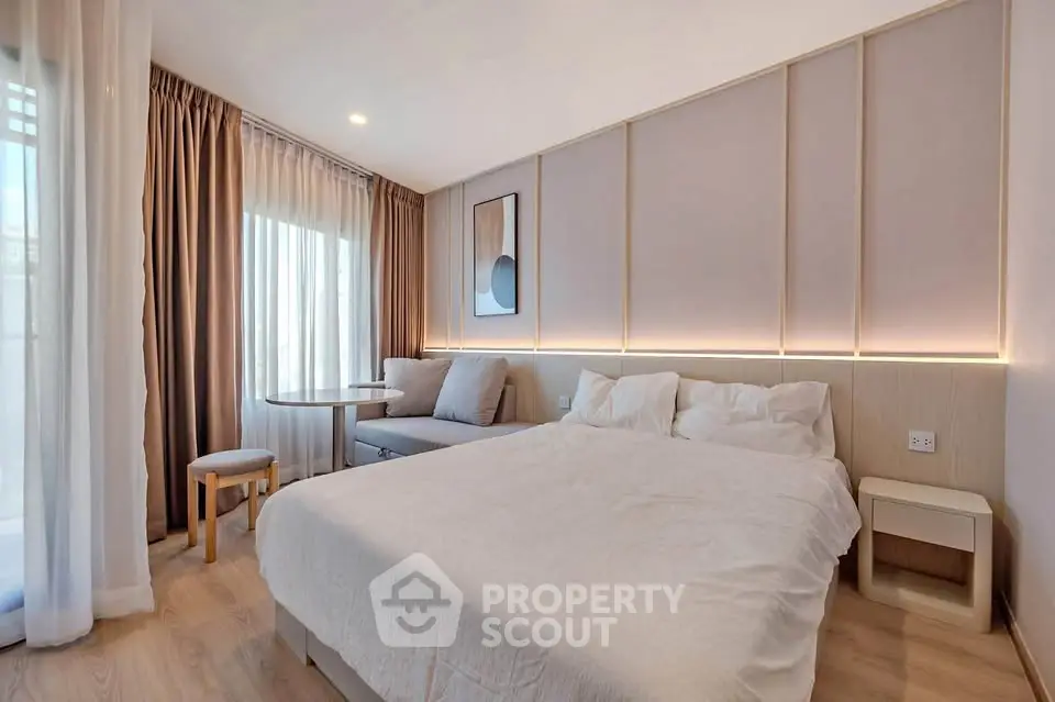 Modern bedroom with elegant decor and natural light, featuring a cozy bed and stylish seating area.