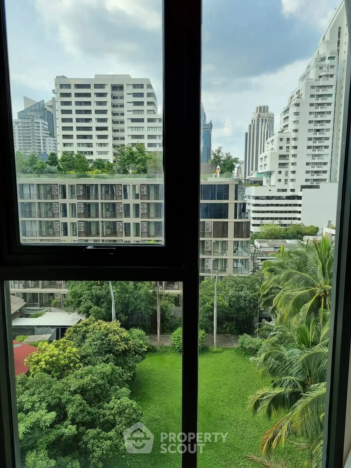 Stunning urban view from high-rise window overlooking lush greenery and modern buildings.