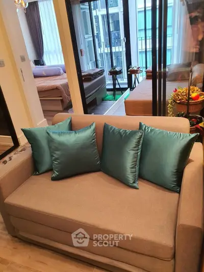 Modern living room with teal cushions and view of bedroom and balcony.