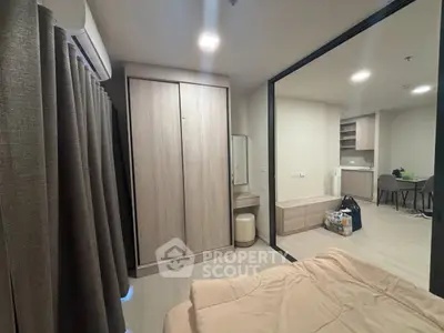 Modern bedroom with sliding glass door and view into open kitchen area, featuring sleek wooden furniture.