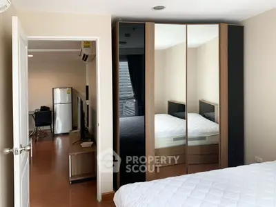 Modern bedroom with mirrored wardrobe and view into living area with fridge and TV.