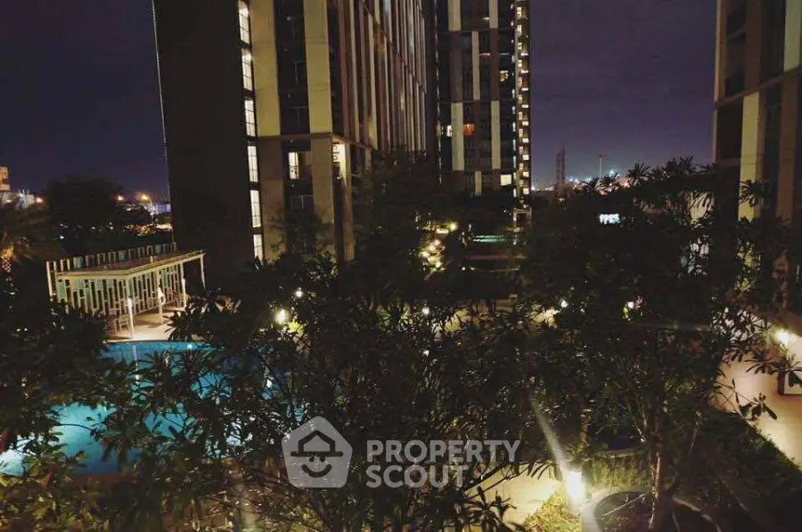 Stunning night view of modern apartment complex with illuminated pool and lush greenery.