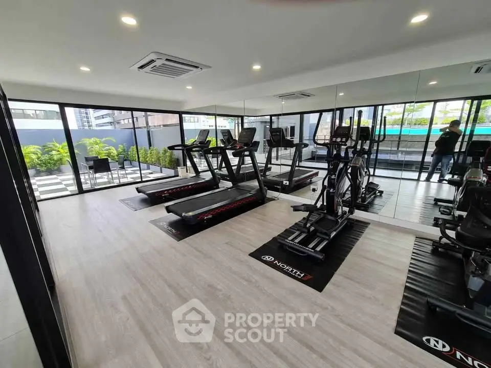 Modern gym with state-of-the-art equipment and floor-to-ceiling windows in luxury building.