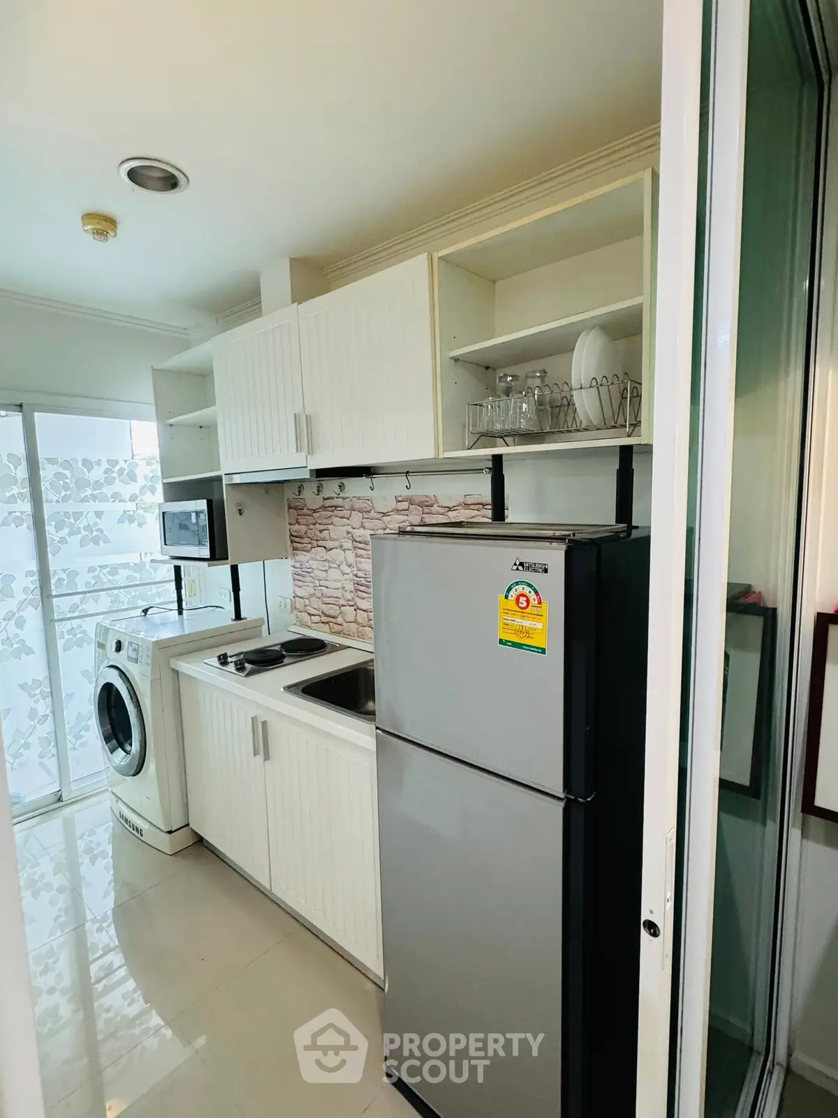Modern compact kitchen with washing machine and fridge in a bright apartment.
