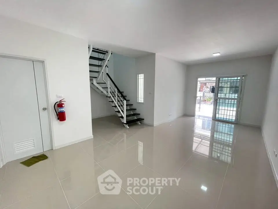 Spacious modern living room with sleek staircase and large windows for natural light.