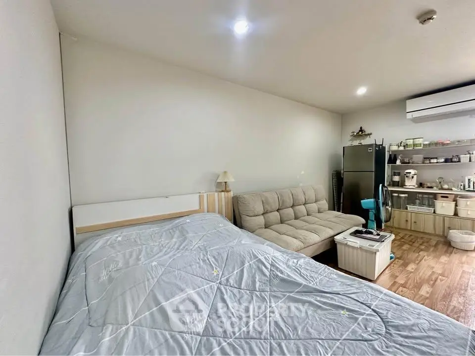 Cozy studio apartment with bed, sofa, and modern kitchen appliances.