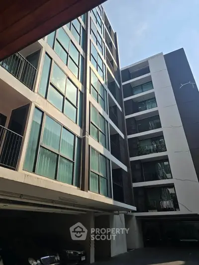 Modern multi-story apartment building with balconies and parking area, showcasing urban living.