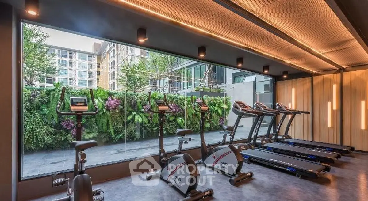 Modern gym with exercise bikes and treadmills overlooking lush greenery in luxury apartment complex.