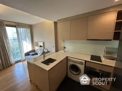 Modern kitchen with open layout and living area, featuring washing machine and sleek appliances.