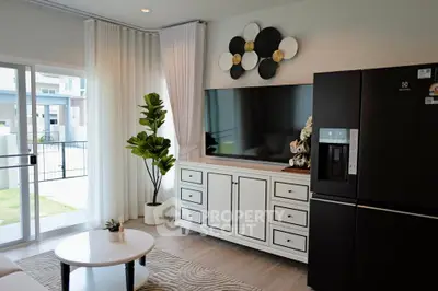 Modern living room with stylish decor and large TV, featuring a sleek black refrigerator and elegant white cabinetry.