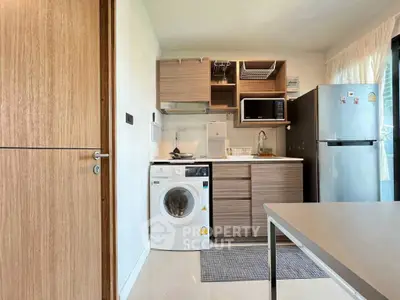 Modern kitchen with washing machine, microwave, and fridge in a compact layout.