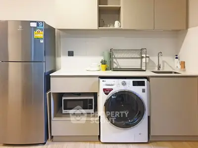 Modern kitchen with stainless steel fridge, washing machine, and microwave in sleek cabinetry.