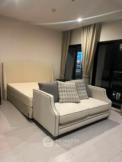 Spacious bedroom with elegant sofa and large windows offering city views.