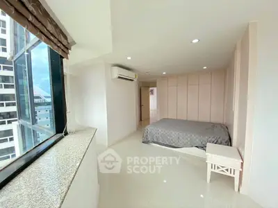Spacious bedroom with large window and modern decor in high-rise apartment