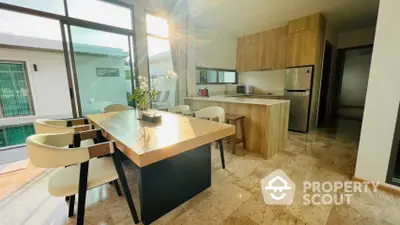 Sunlit open-plan kitchen with modern wooden cabinetry and spacious dining area, featuring large windows and elegant flooring.