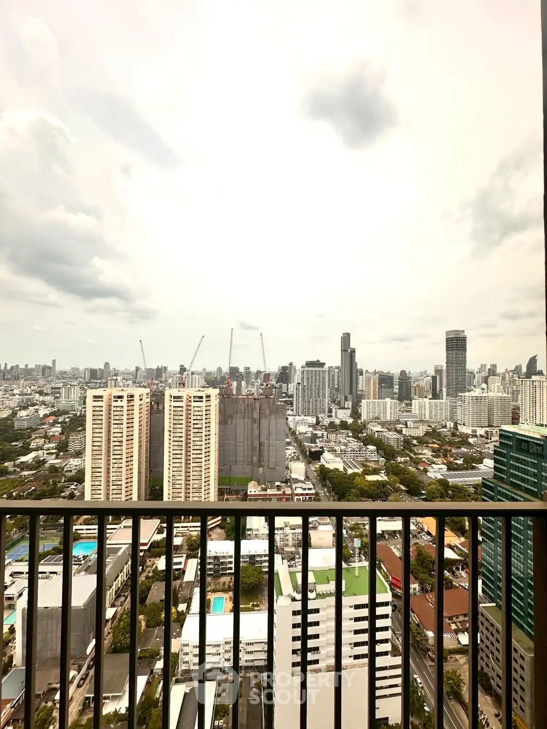 Stunning cityscape view from a high-rise balcony showcasing urban skyline and construction cranes.