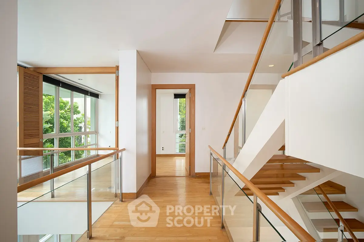 Modern multi-level home interior with wooden floors and glass railings, showcasing open and airy design.