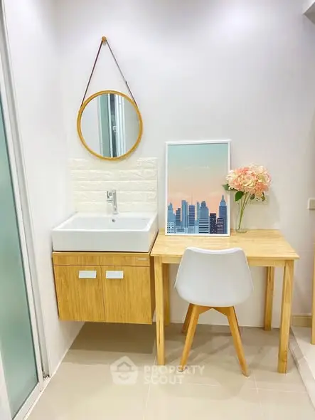 Modern bathroom with stylish vanity and wooden desk, featuring a round mirror and decorative artwork.