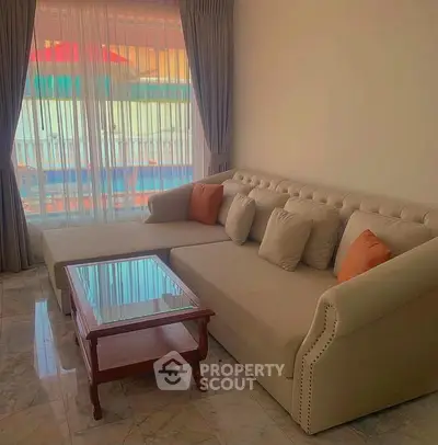Elegant living room with plush beige sofa and glass coffee table, featuring large window with city view.