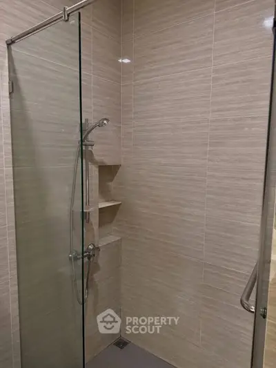 Modern bathroom with sleek glass shower enclosure and beige tiled walls.