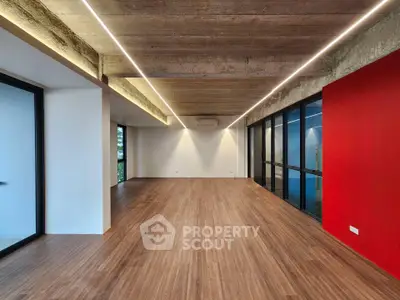 Spacious modern interior with wooden flooring and red accent wall, ideal for versatile living or office space.